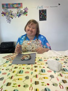 Woman with learning disability smiling and painting rock